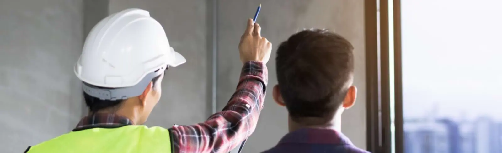 Ein Handwerker zeigt auf eine Wand, spricht Problemfelder an und bespricht eine Innendämmung aus Calciumsilikatplatten